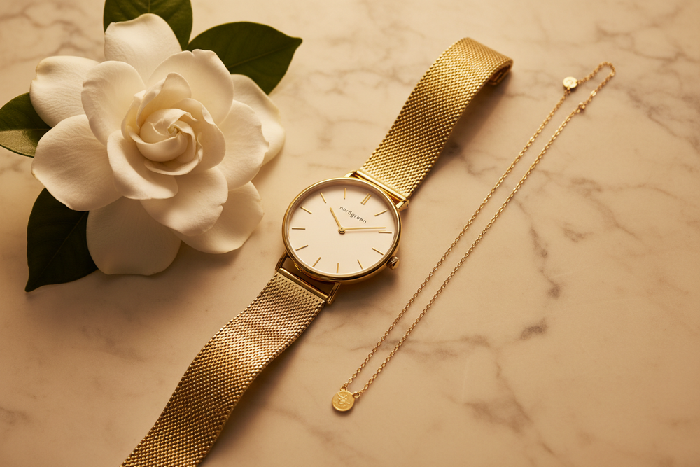 Nordgreen Native 28mm Gold Mesh Dress Watch flat lay on ivory marble with white gardenia